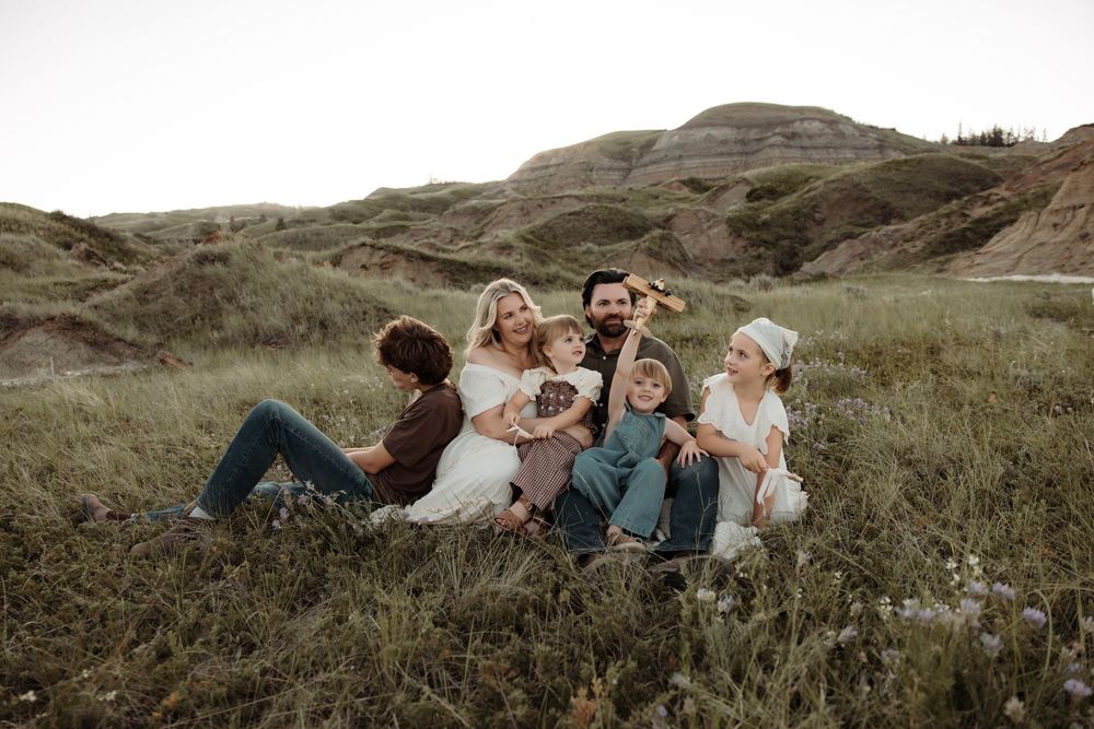 Family of six sitting together in a grassy valley with rolling hills in the background.