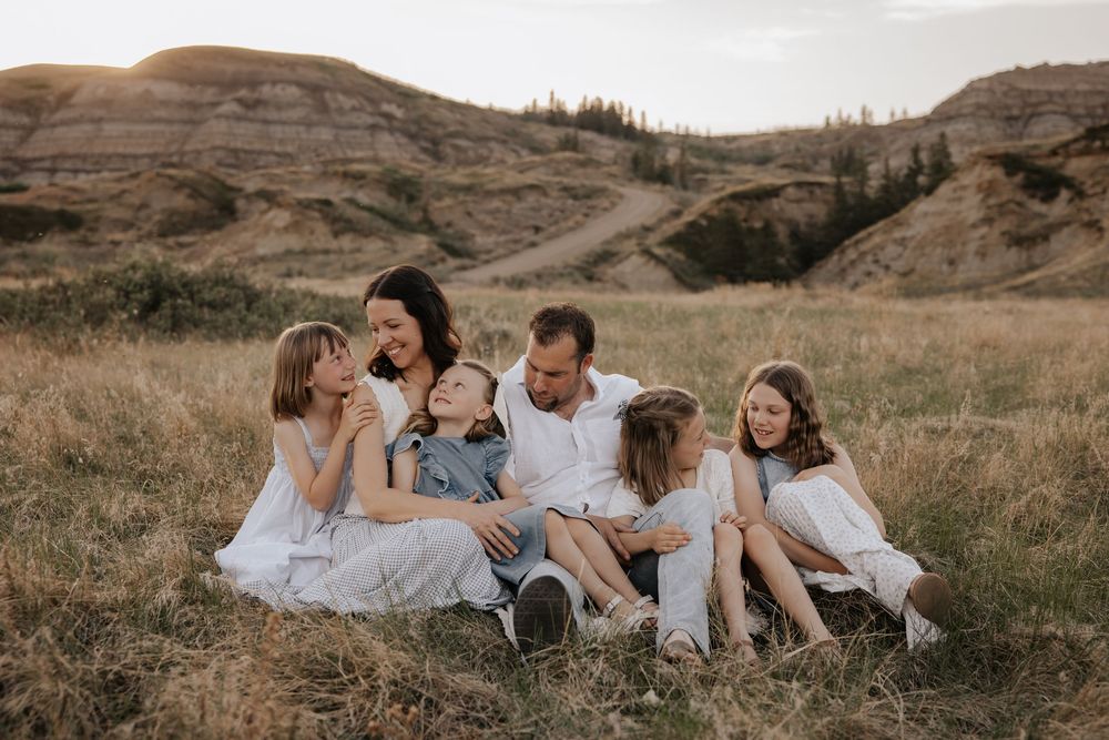 Family of six sitting together in golden grass field at dry buffalo jump for their family photoshoot in alberta