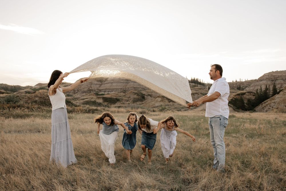 Family of five playing with a flowing sheer fabric in a golden field at sunset in calgary alberta for their family photoshoot