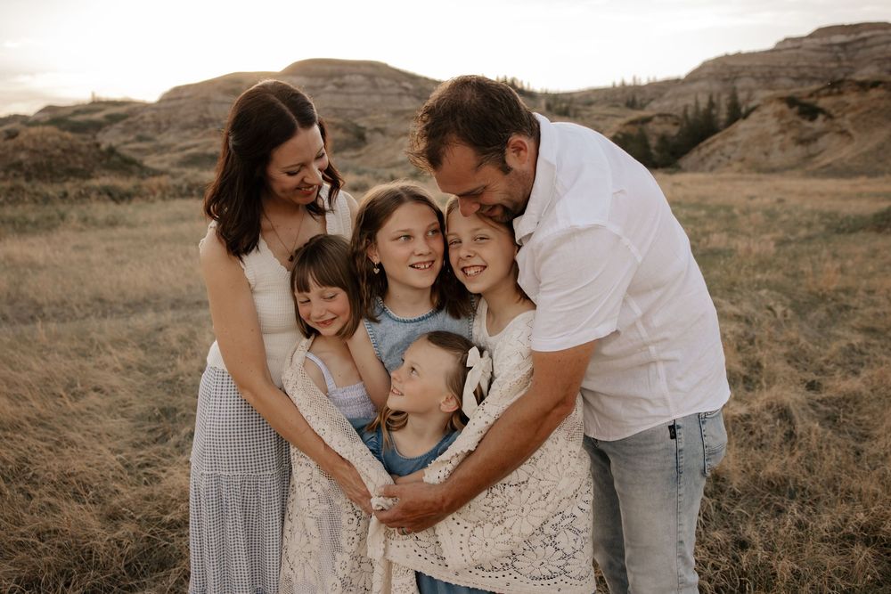 Family of five embracing outdoors in golden field with rolling hills, during family photography shoot