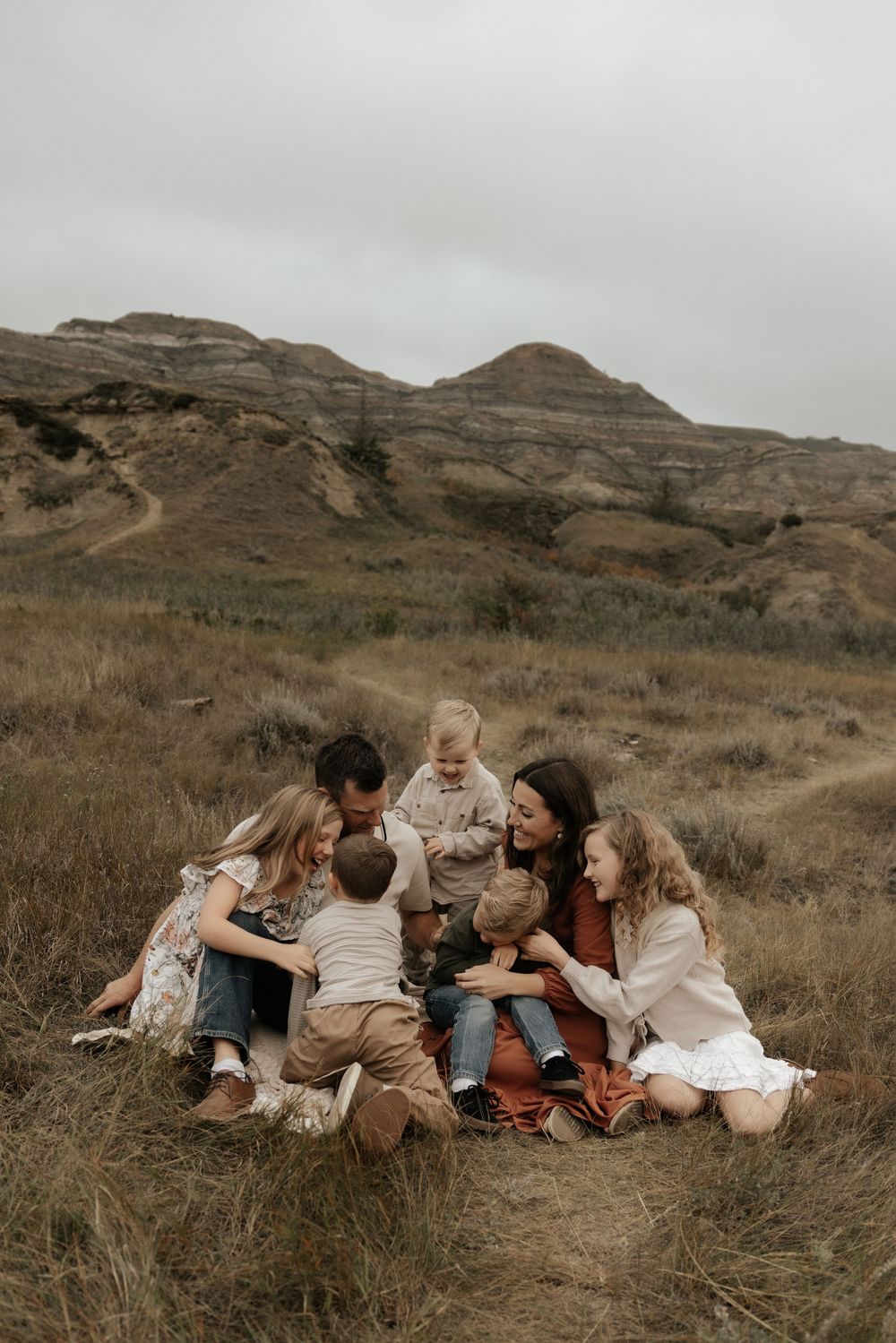 A joyful family of seven sits together in the middle of Albertas badlands laughing together as they tickle