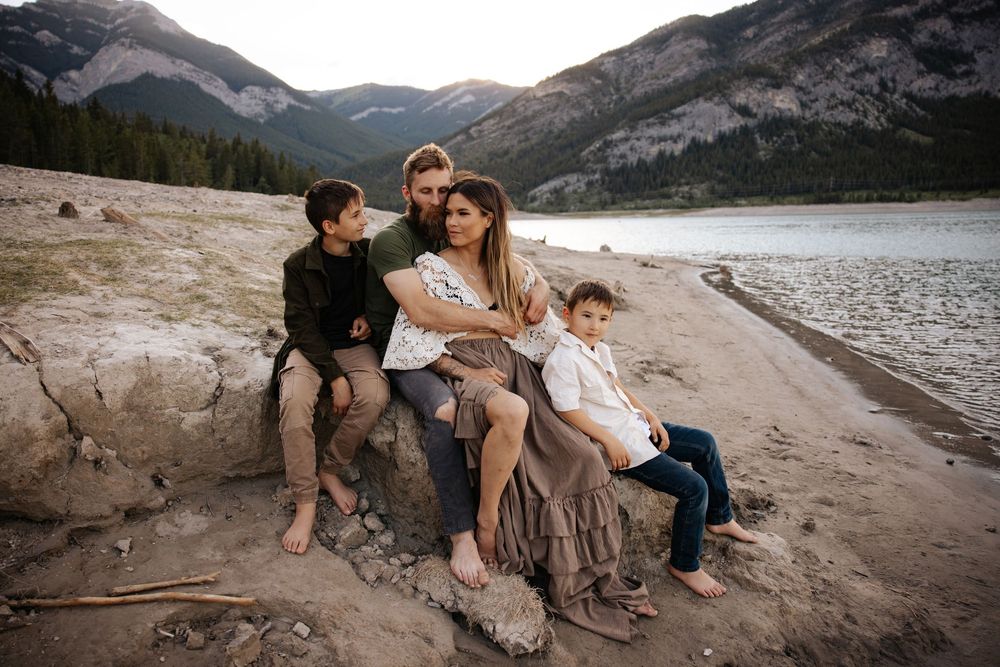 Family exploring rocky lakeside terrain with mountain views in the background at barrier lake alberta for a family photography shoot