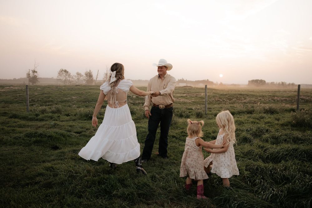 a country wester family with two young girls in a misty green field at sunset on a farm play during a family photography shoot