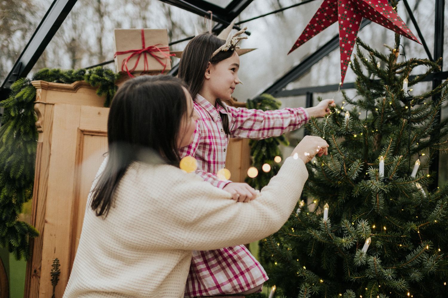 Two people decorating a Christmas tree together with ornaments and a red star topper in a cozy indoor setting.