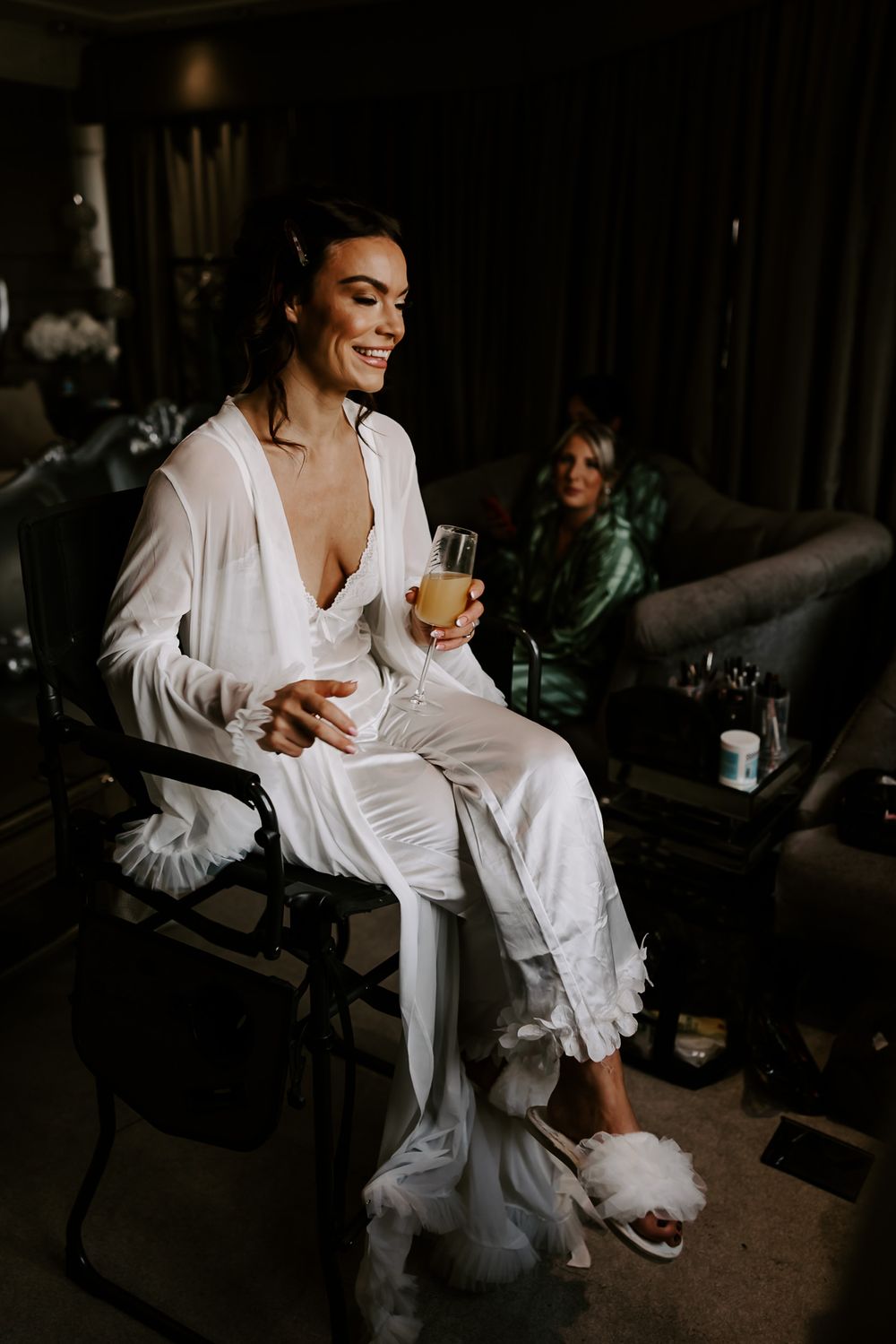 A person in a white robe relaxes in a dimly lit room while holding a drink.