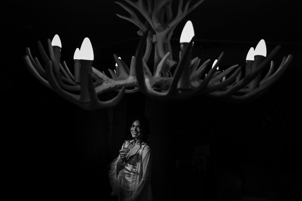 A dramatic black and white photograph under an illuminated antler chandelier creating a moody atmosphere.