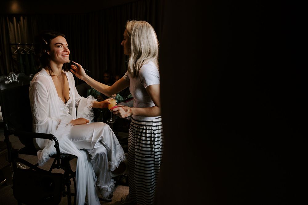 A person in a white shirt getting their makeup done in a dark room with dramatic lighting.