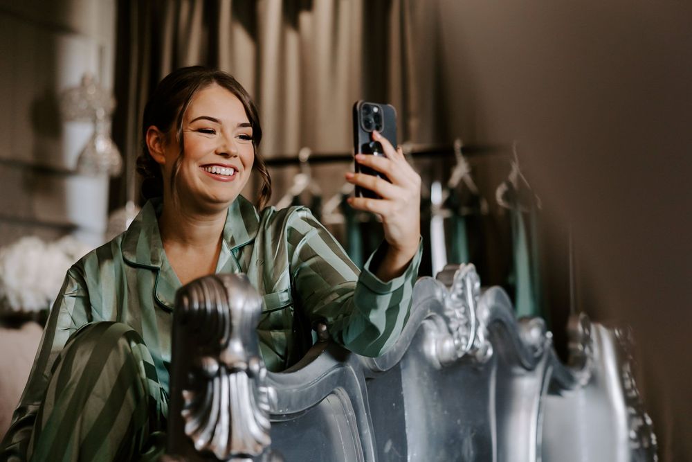 Person in green jacket laughing while sitting near window with natural light streaming in.