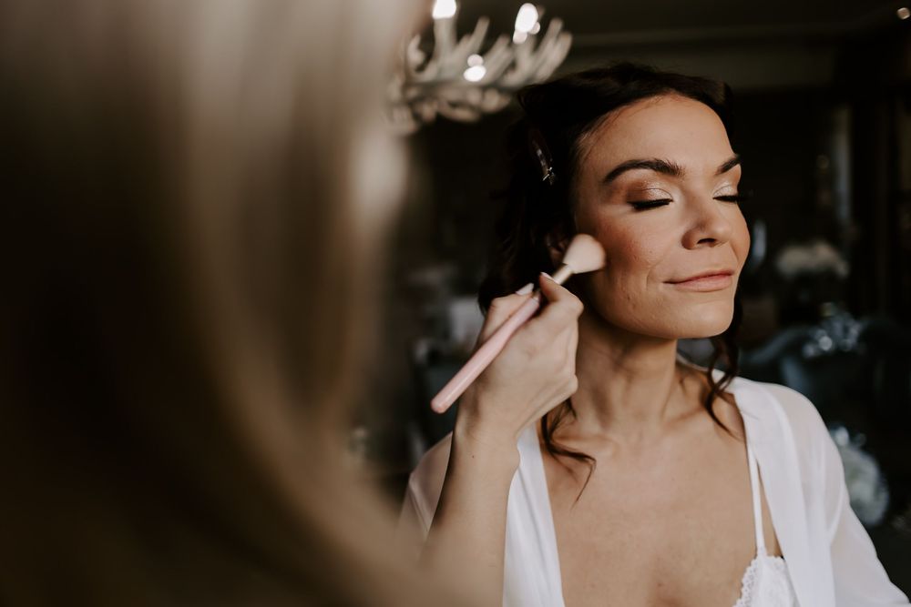 A bride in a white wedding dress touches her face while getting ready for her wedding ceremony.