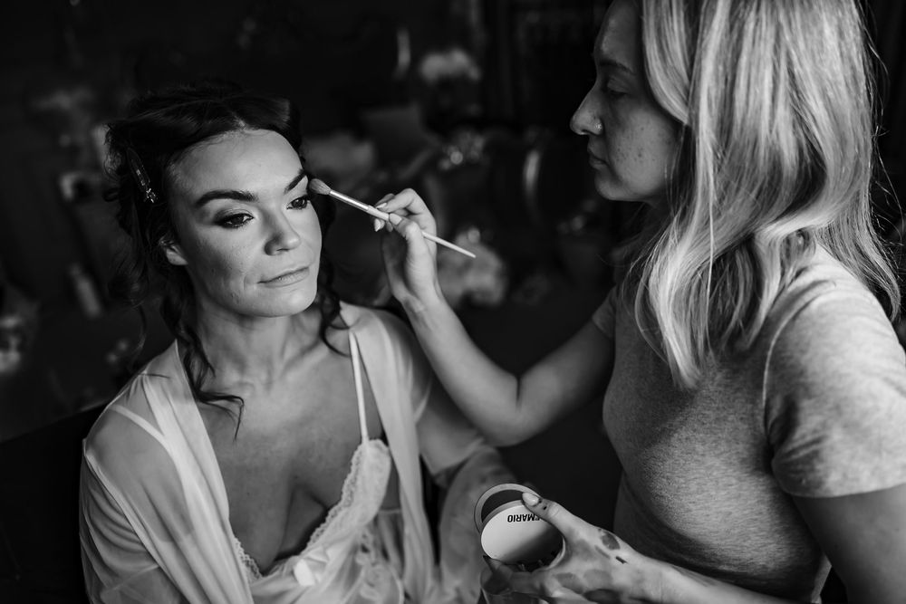 A makeup artist applies cosmetics to a person in a white shirt during a professional beauty session.
