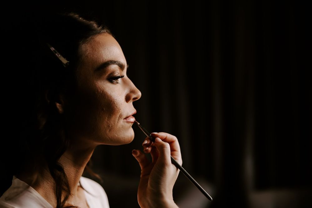 Professional makeup artist applies cosmetics with brush in dramatic lighting against dark background.