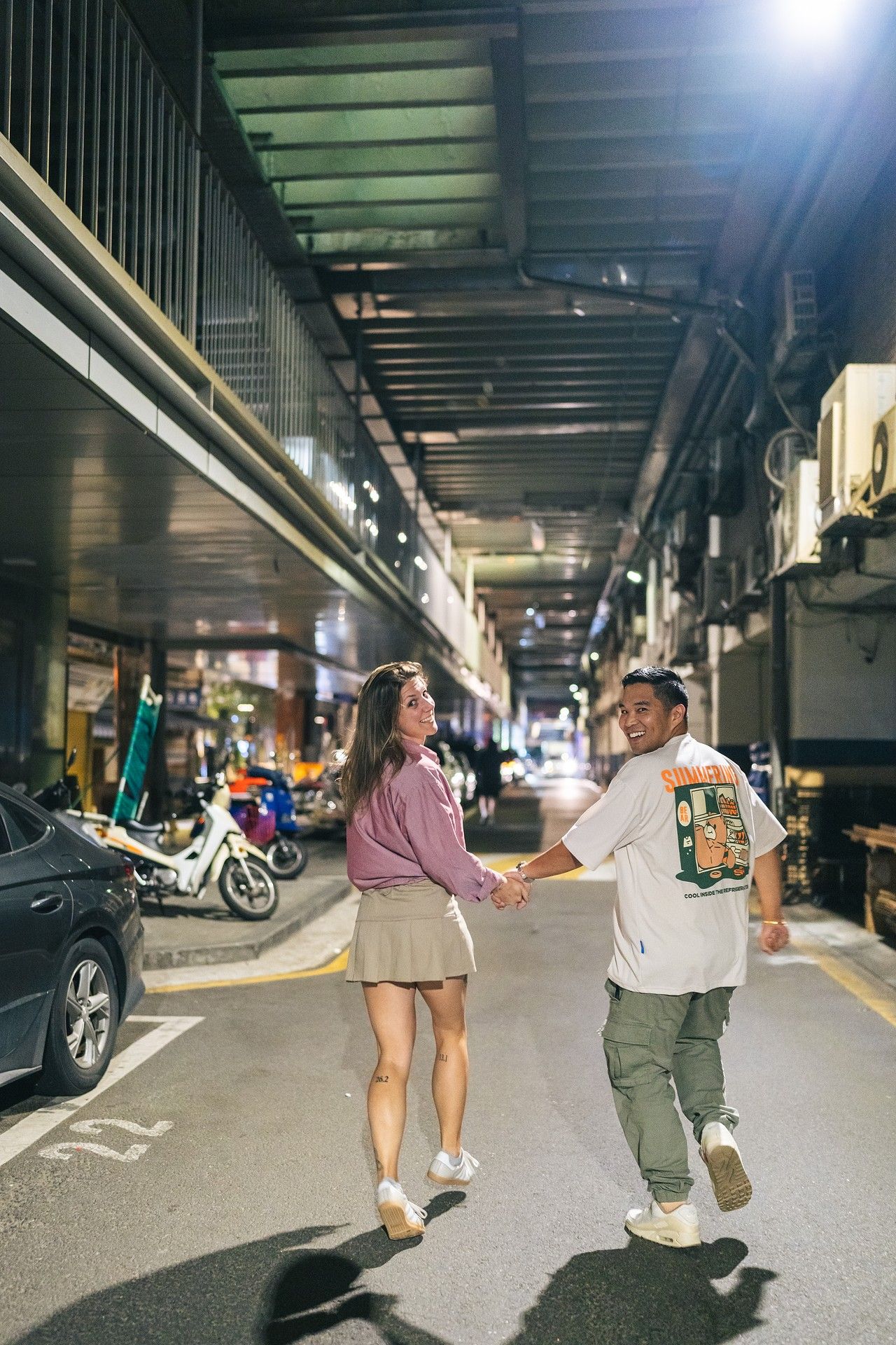 Two people playfully dance and spin together in a dimly lit parking garage at night.