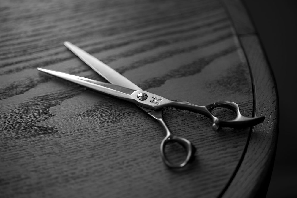 Professional hairdressing scissors with silver metal blades resting on dark wooden surface in black and white.