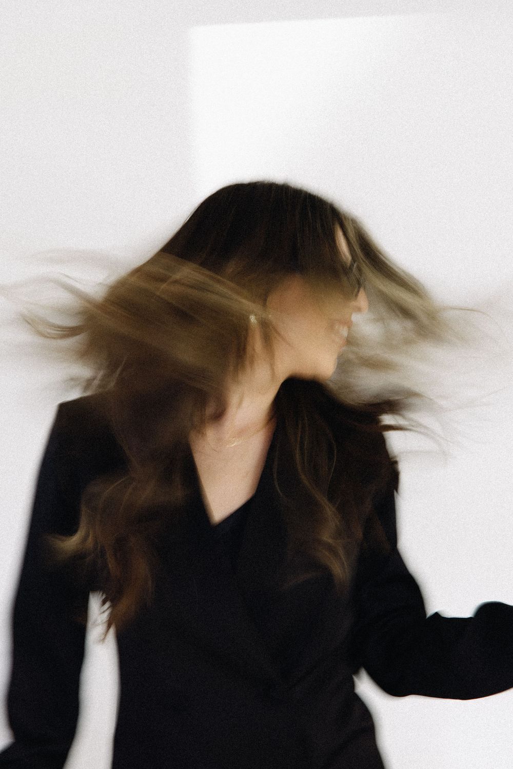 Motion blur portrait of someone with long brown hair wearing black, creating a dynamic hair-flipping effect.
