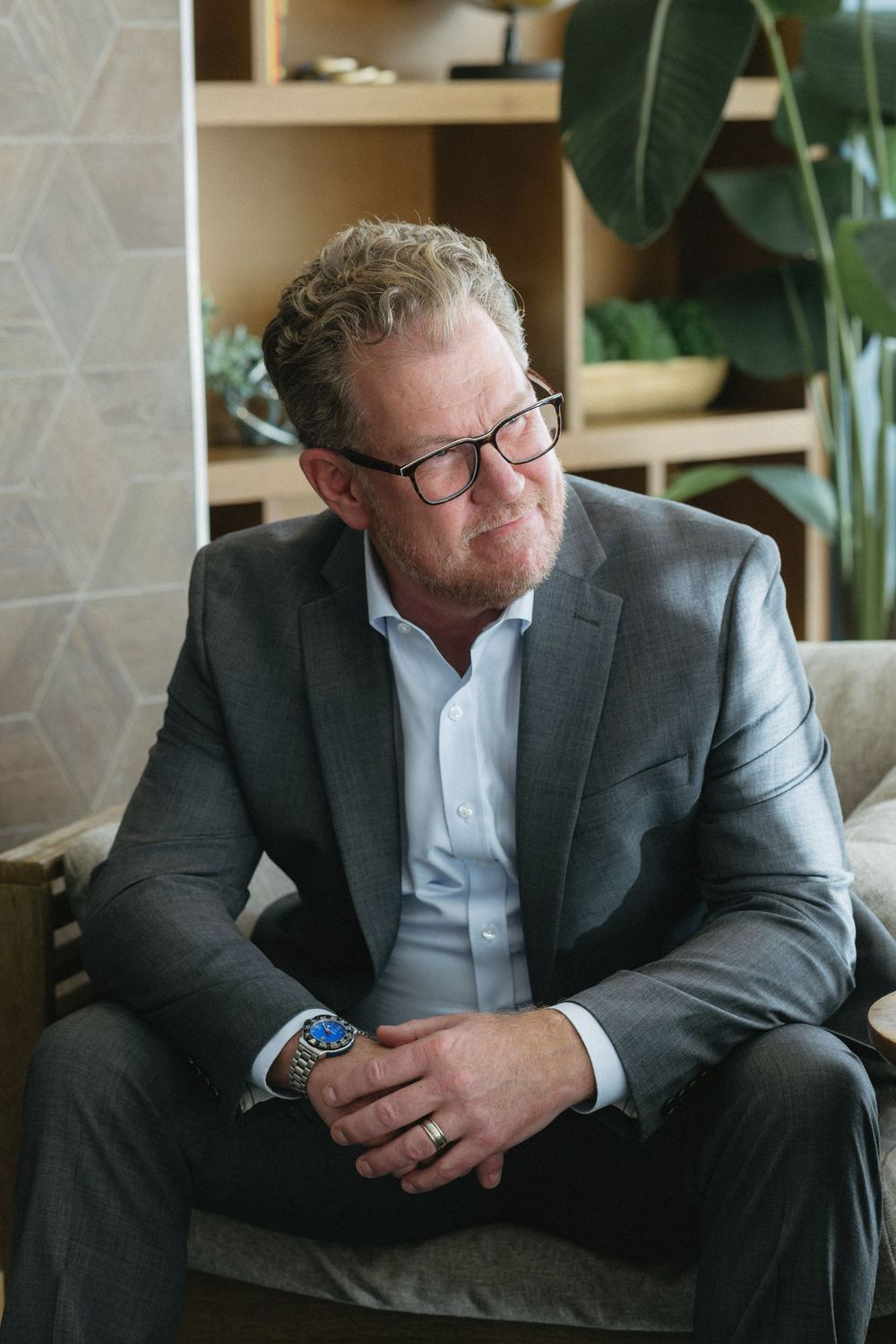 Person in business attire seated looking down at phone in modern interior setting.