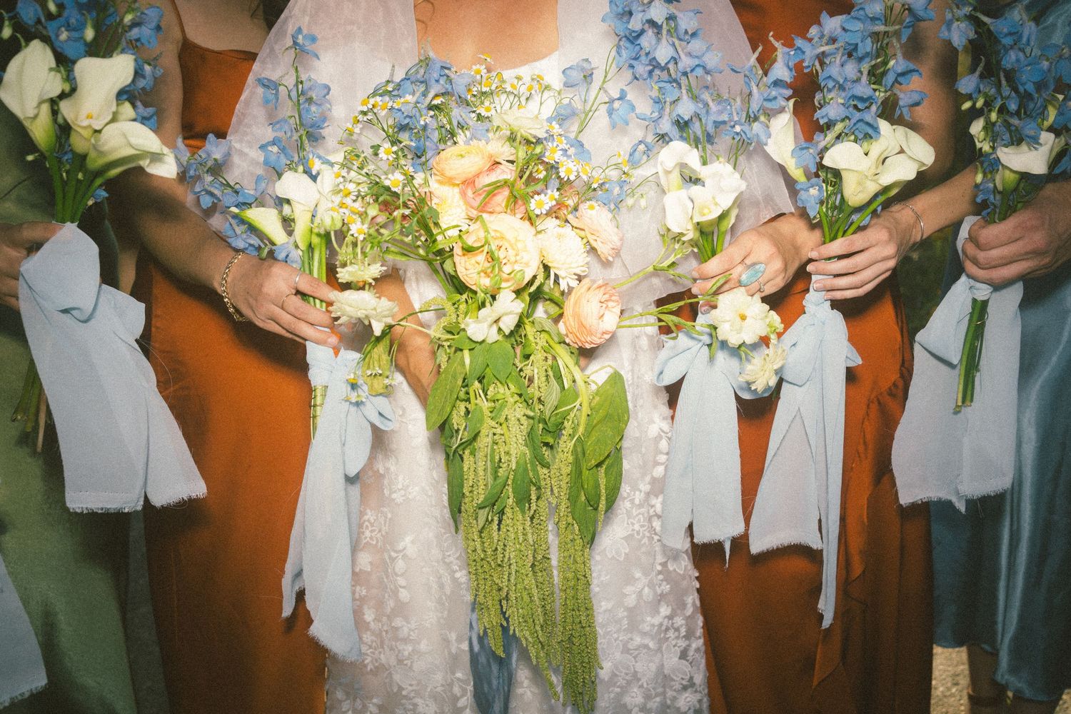 Elegant wedding bouquets with white flowers and flowing ribbons held against light blue dresses at a bridal ceremony.