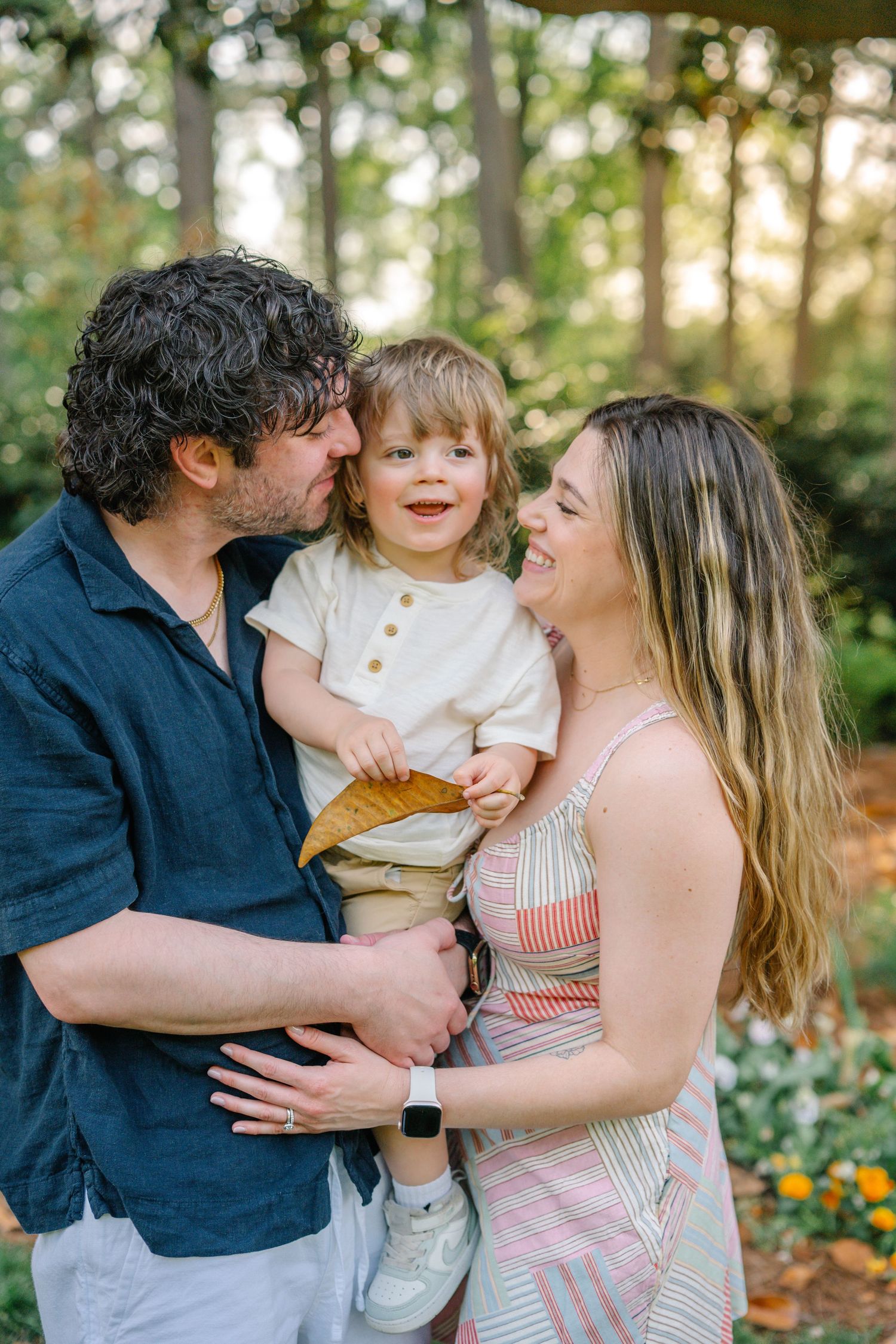Happy young family with toddler child smiling together in a sunlit garden.