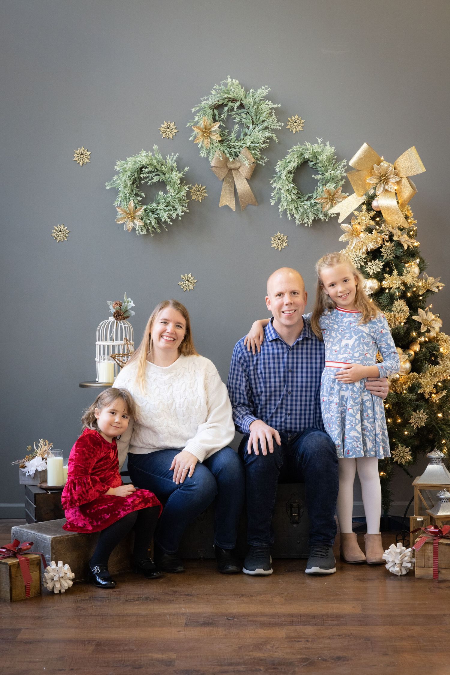 Family wearing matching navy and plaid Christmas pajamas and red slippers pose together by holiday decorations.