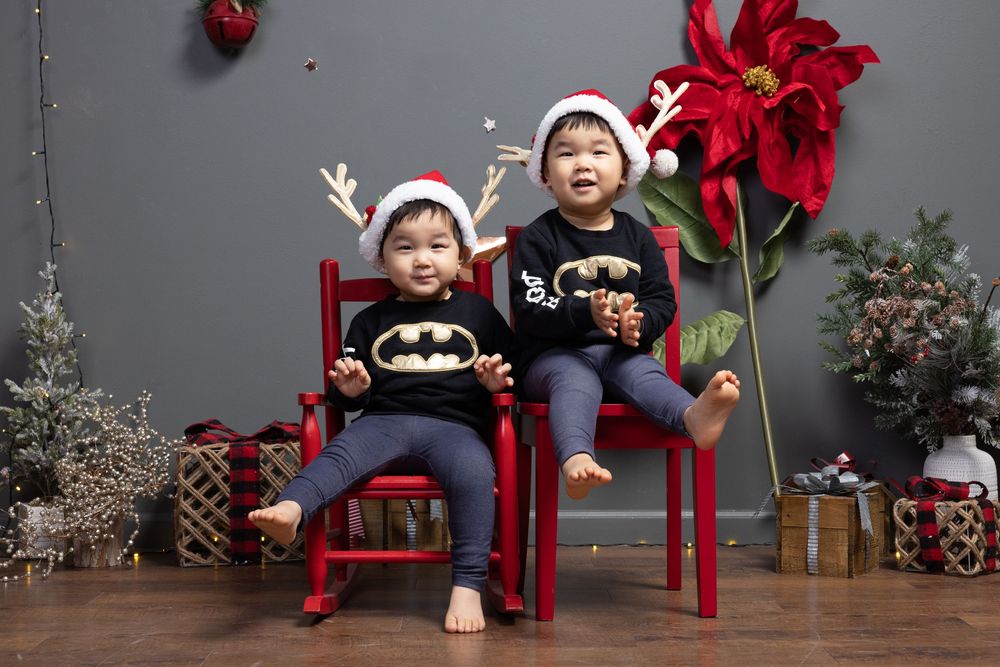 A festive holiday photo session setup with red chairs and Christmas decorations against a grey backdrop.