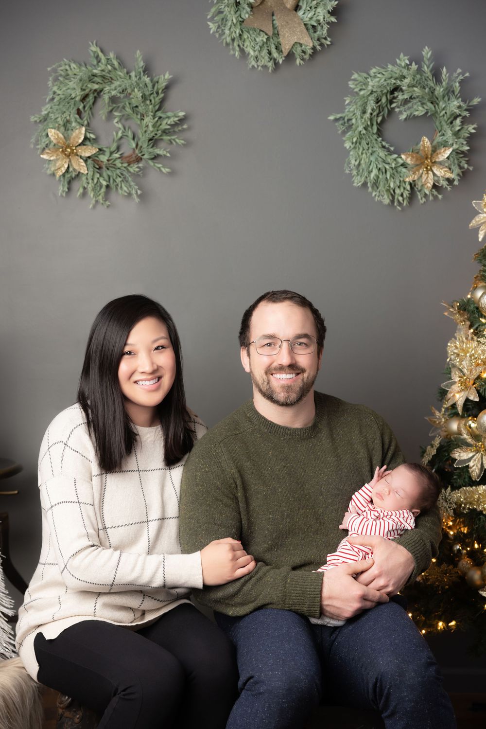 A family sits together on a couch against a grey wall decorated with holiday wreaths and gold stars.