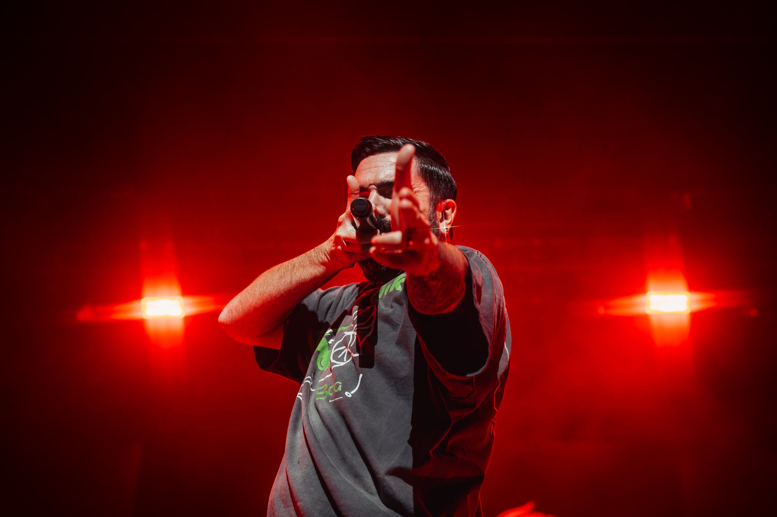 Performer singing passionately on stage with dramatic red lighting and lens flares in the background.