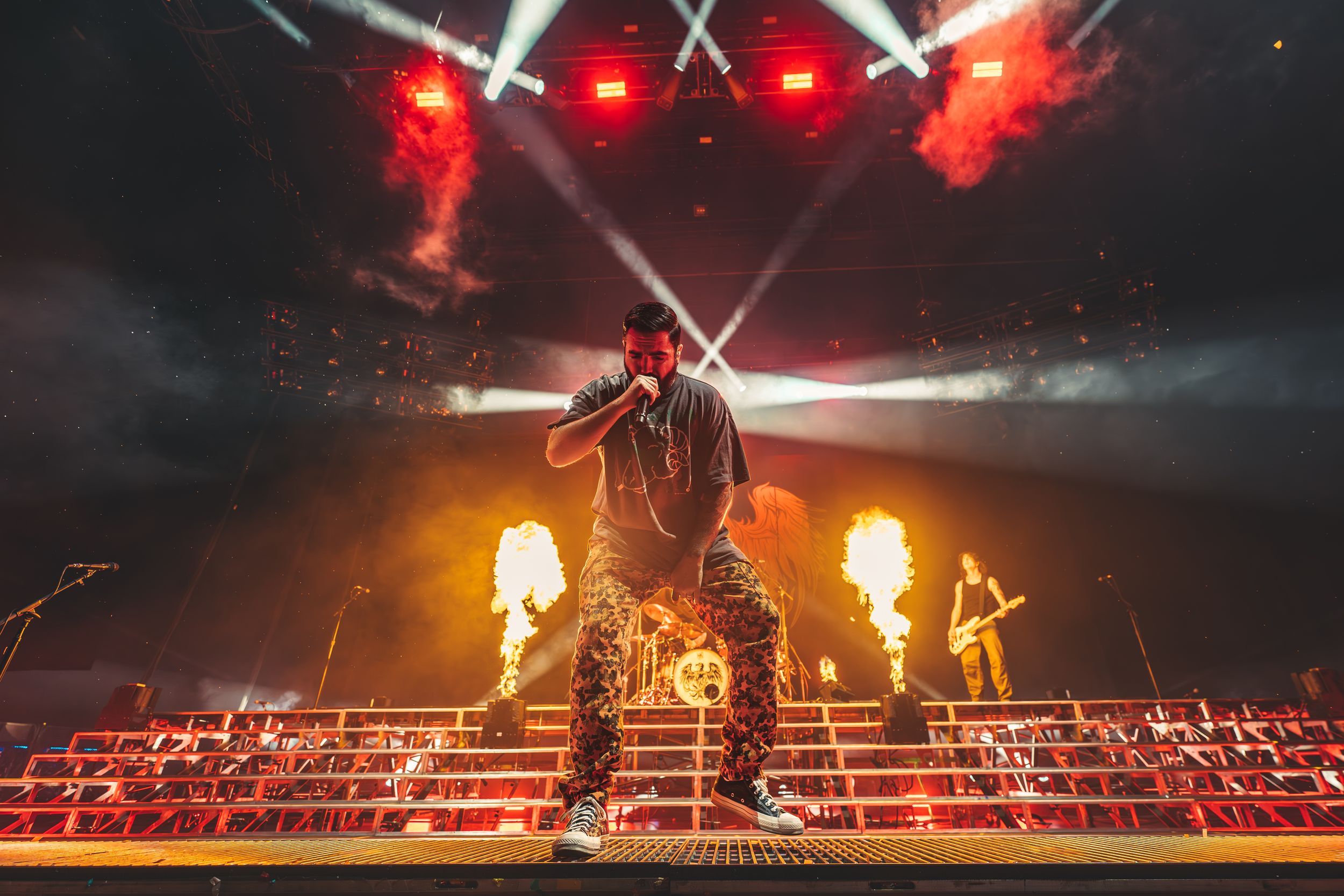 Concert stage illuminated with dramatic red lighting and pyrotechnic effects during an energetic live performance.