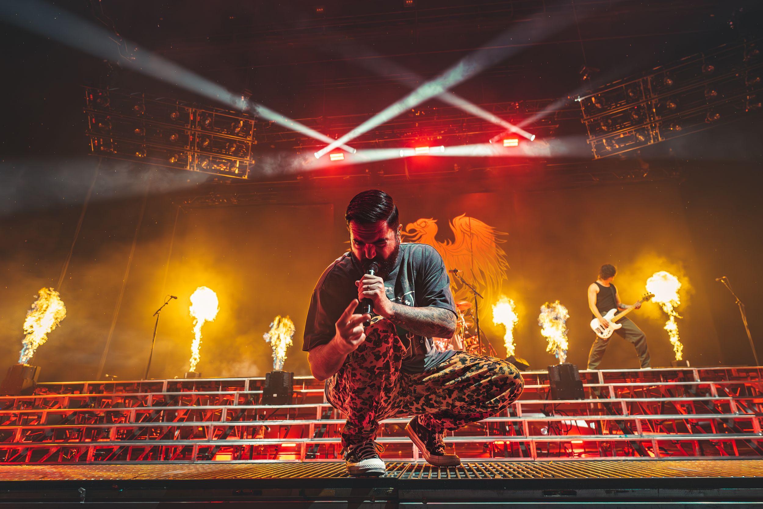 Concert stage performance with fire effects, red stairs and crossed light beams creating dynamic atmosphere.