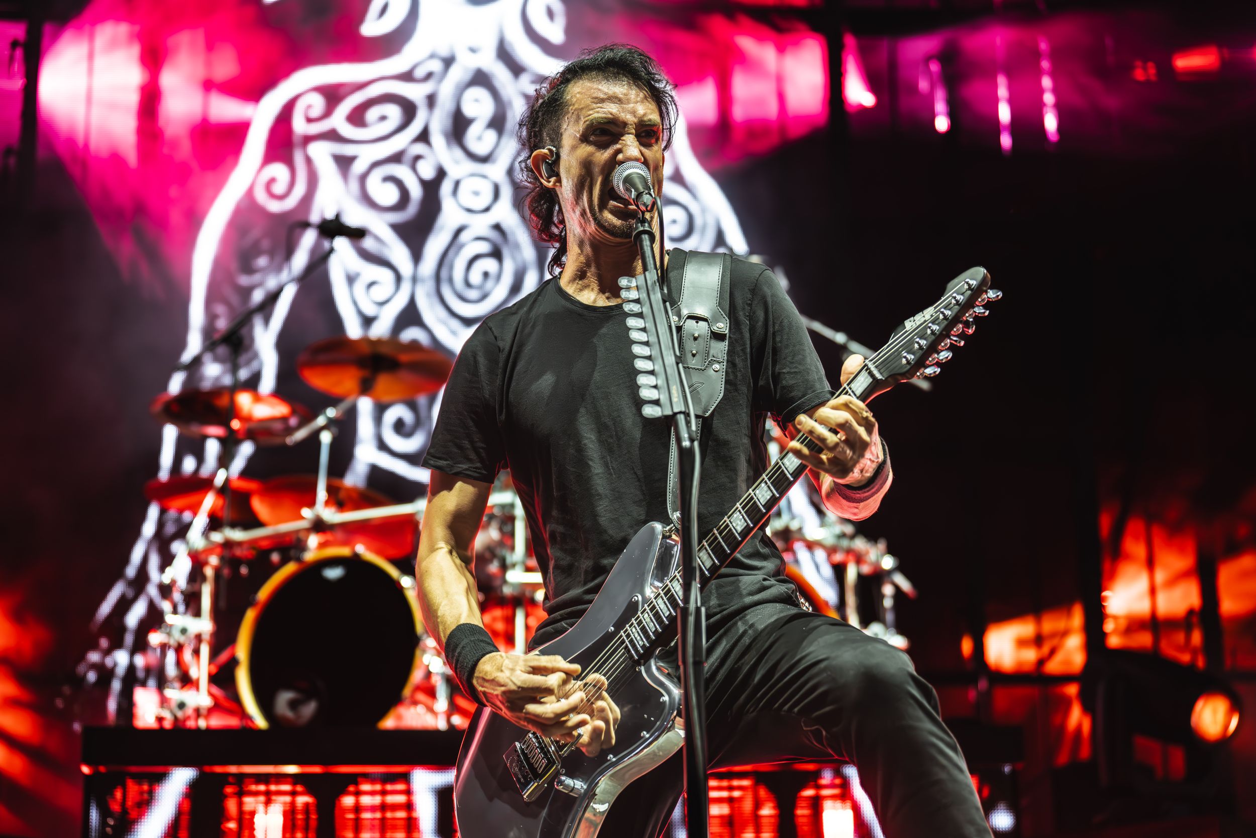 Rock band performs energetically on stage with bright red lighting and dramatic effects during a live concert performance.