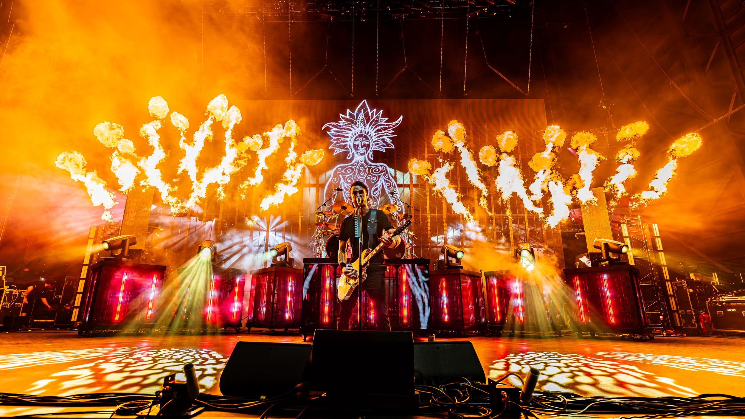Spectacular concert stage with vibrant orange lighting and pyrotechnics creating a dramatic atmosphere during live performance.
