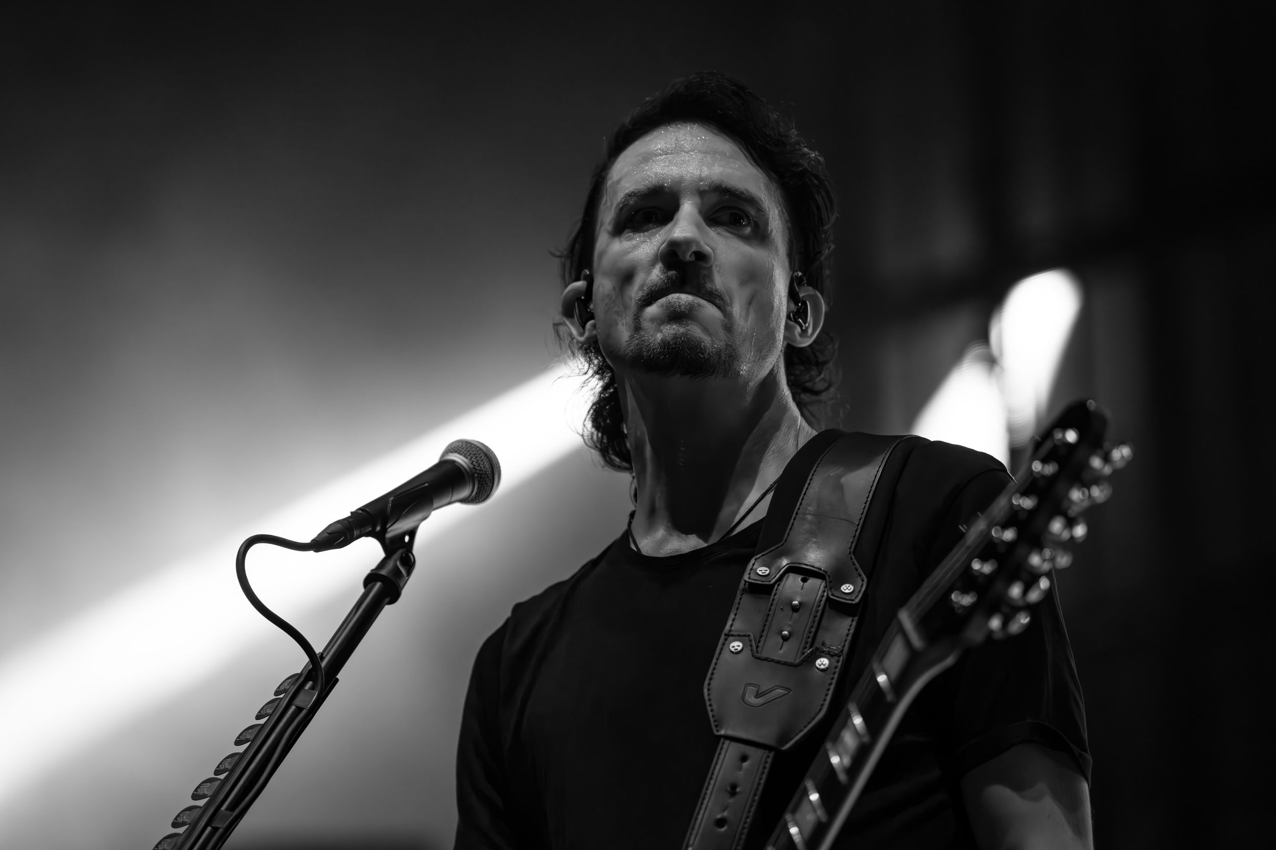 Black and white photo of a guitarist performing on stage with dramatic lighting and shadows.