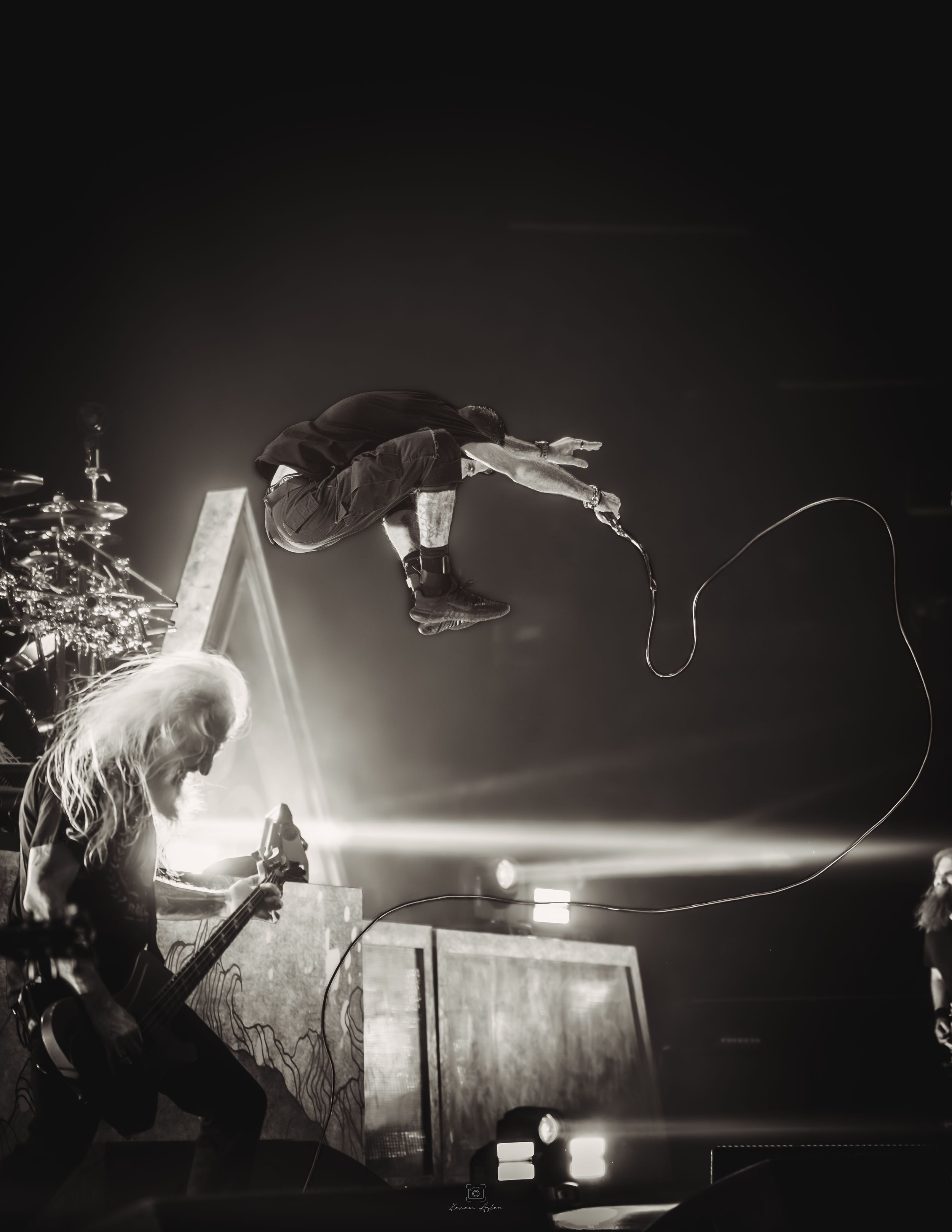 Dramatic black and white concert photo showing silhouetted performers on stage with bright backlighting and fog effects.
