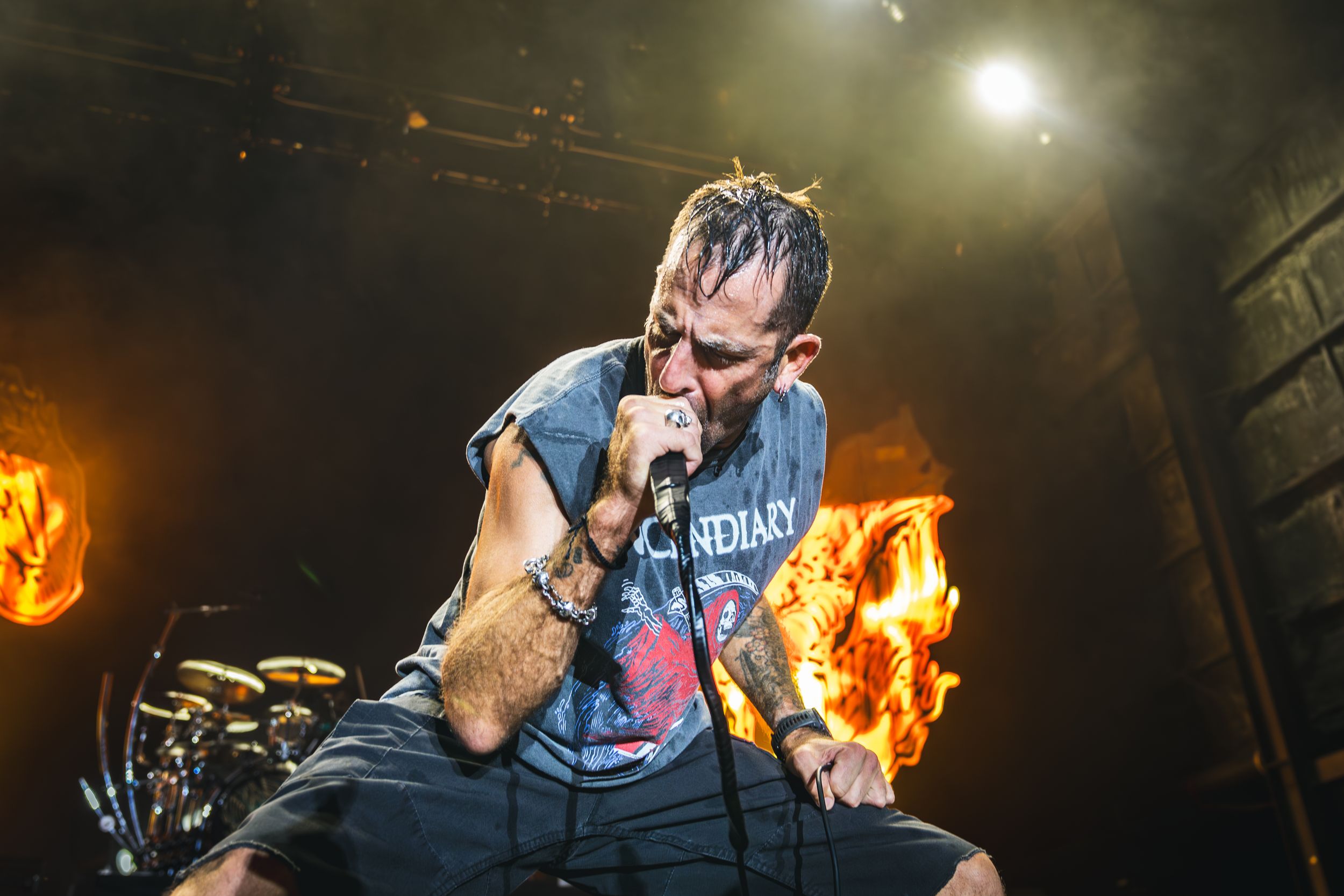 Metal band vocalist performs on stage with dramatic fire and lighting effects in dark concert setting.