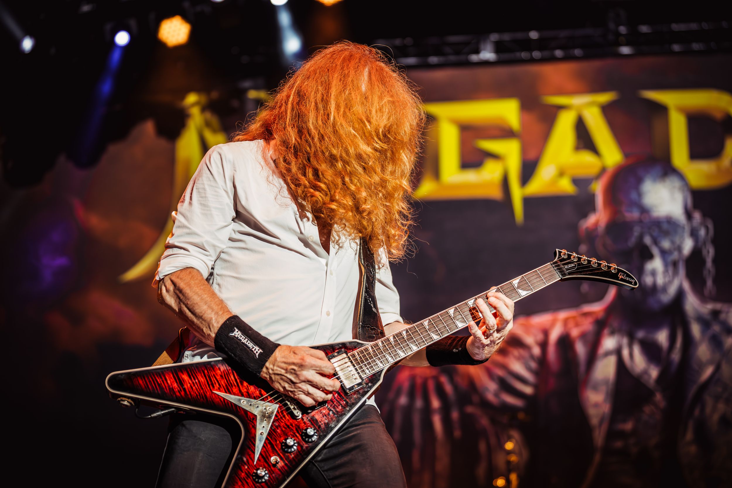 Guitarist performs on stage with a red electric guitar under dramatic concert lighting.