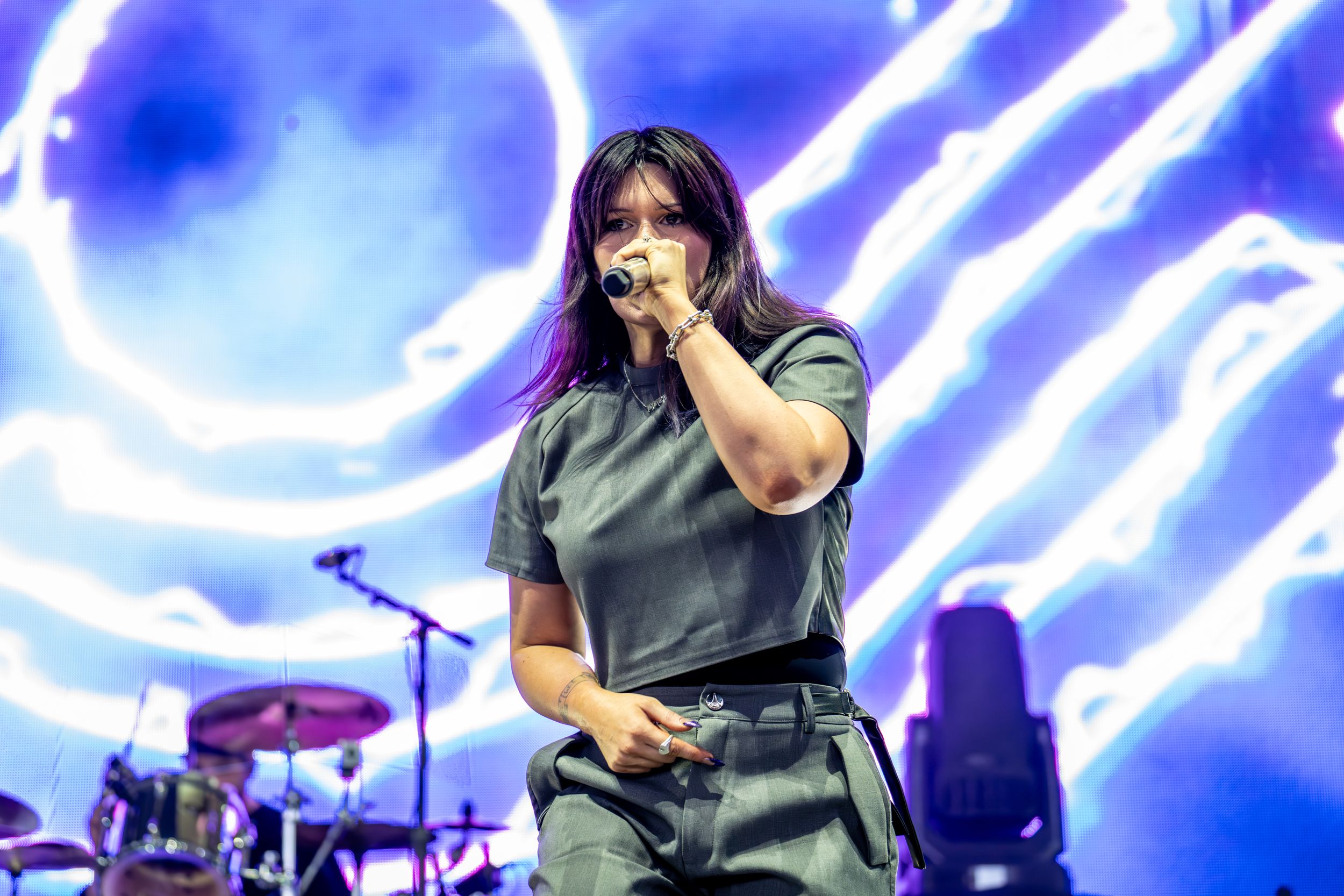 A performer sings on stage with a dramatic blue and white light display behind them during a concert performance.