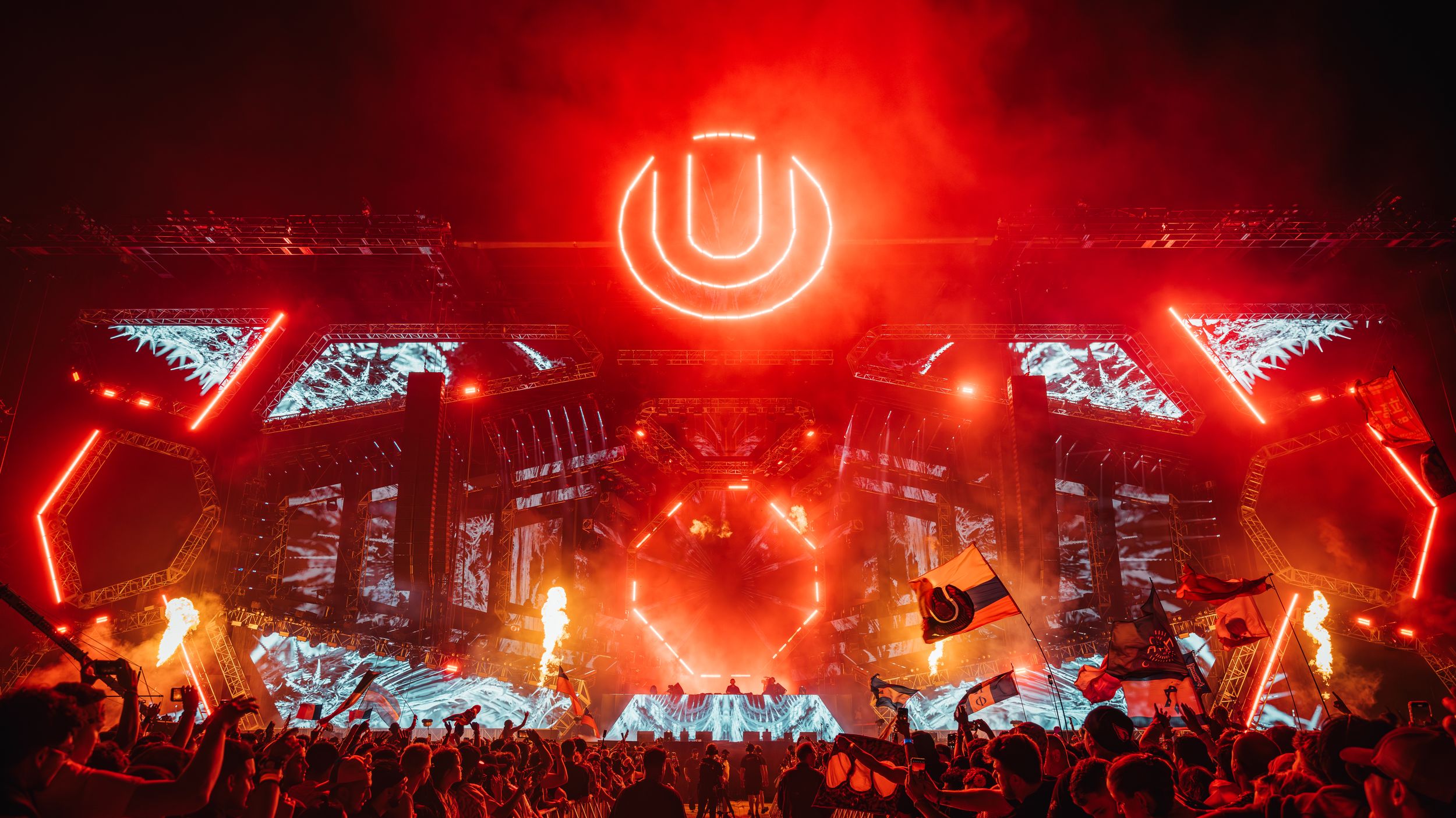 Concert stage illuminated with vibrant red lighting and neon signs creates an electrifying atmosphere during live performance.