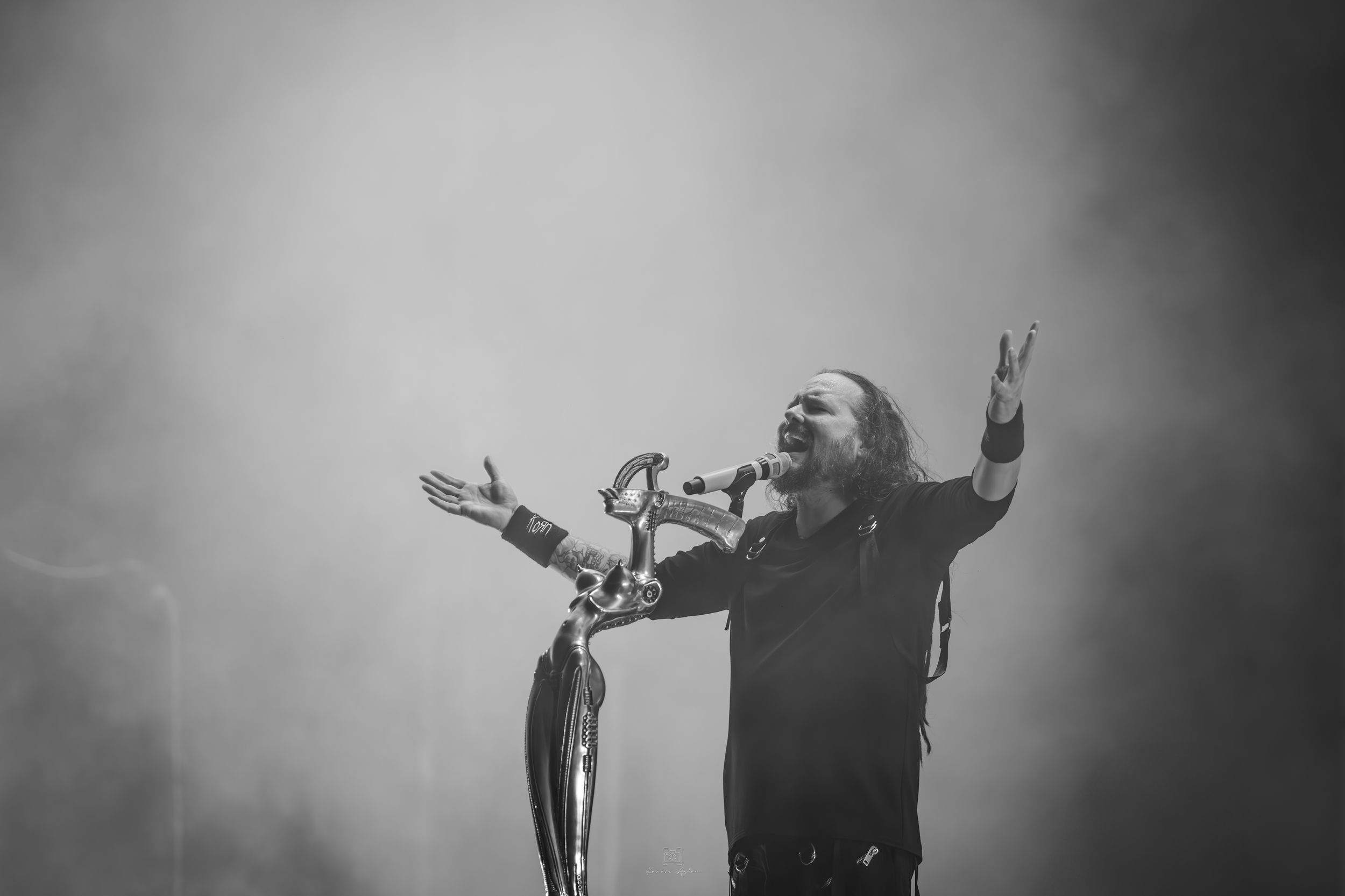 Silhouetted figures perform on a concert stage with dramatic backlighting and fog effects creating a moody atmosphere.