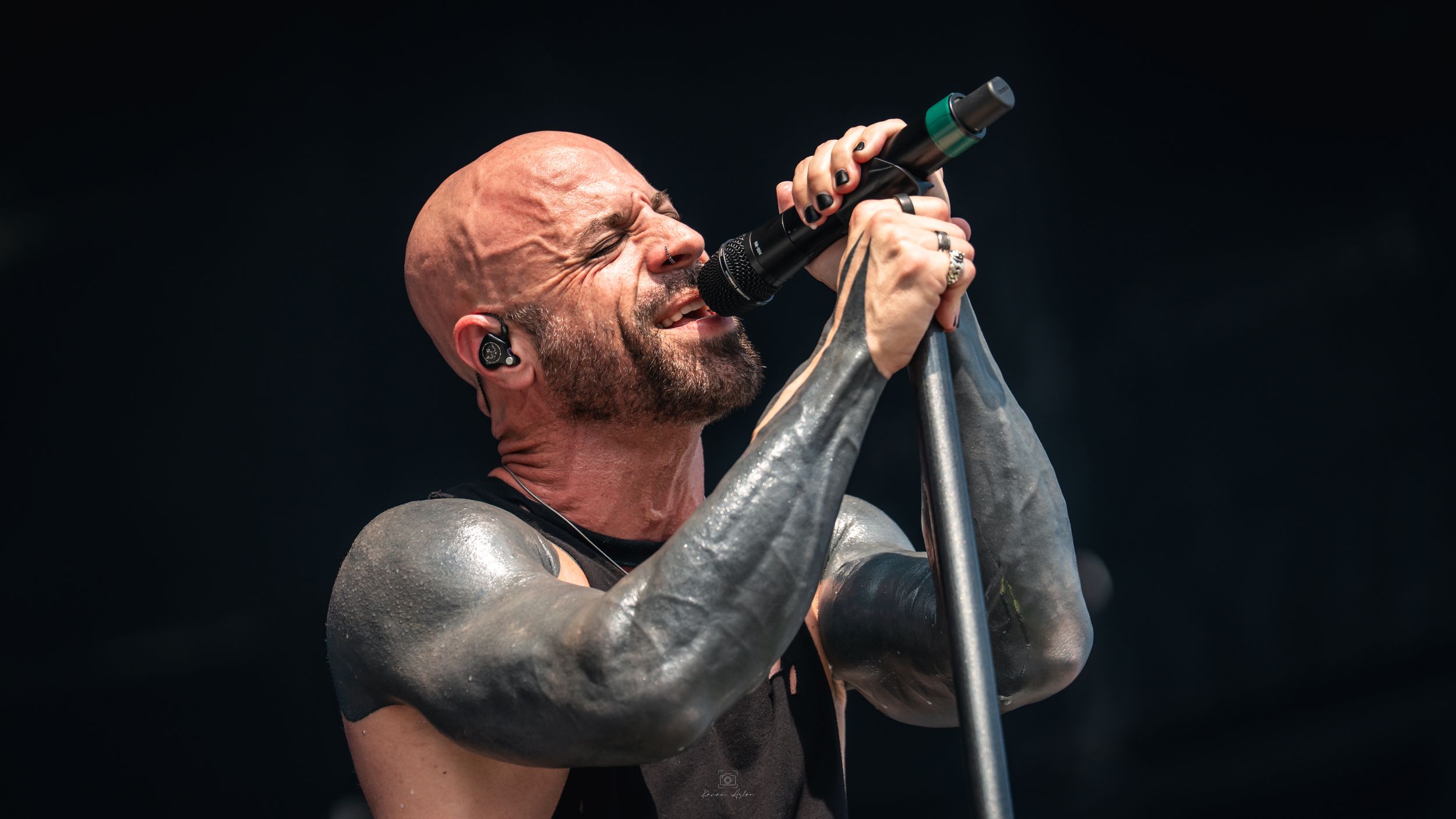 A passionate performer singing intensely into a microphone on a dark stage during a concert performance.