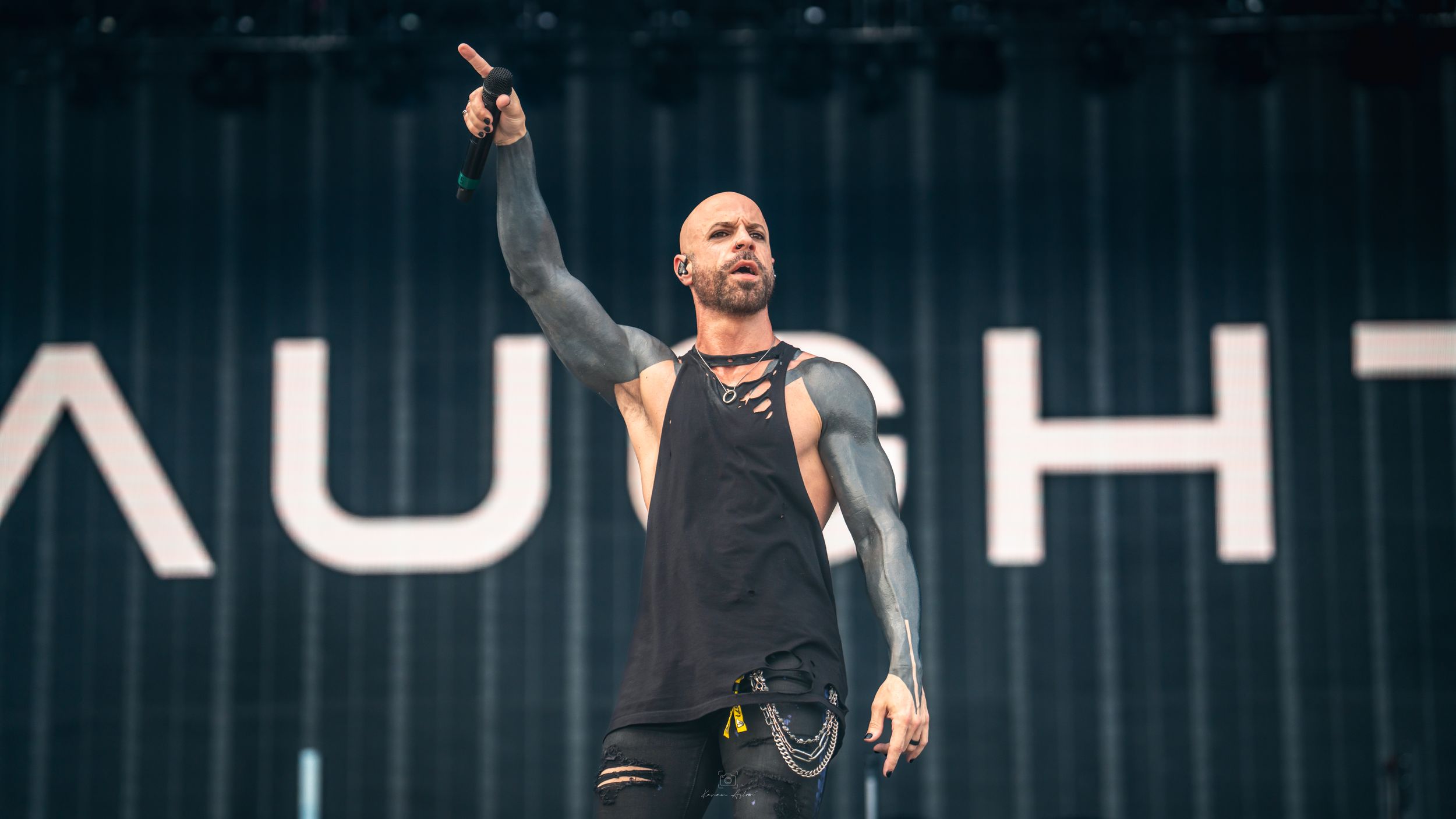 A performer on stage gestures with their arms raised during a dramatic concert performance in dark lighting.