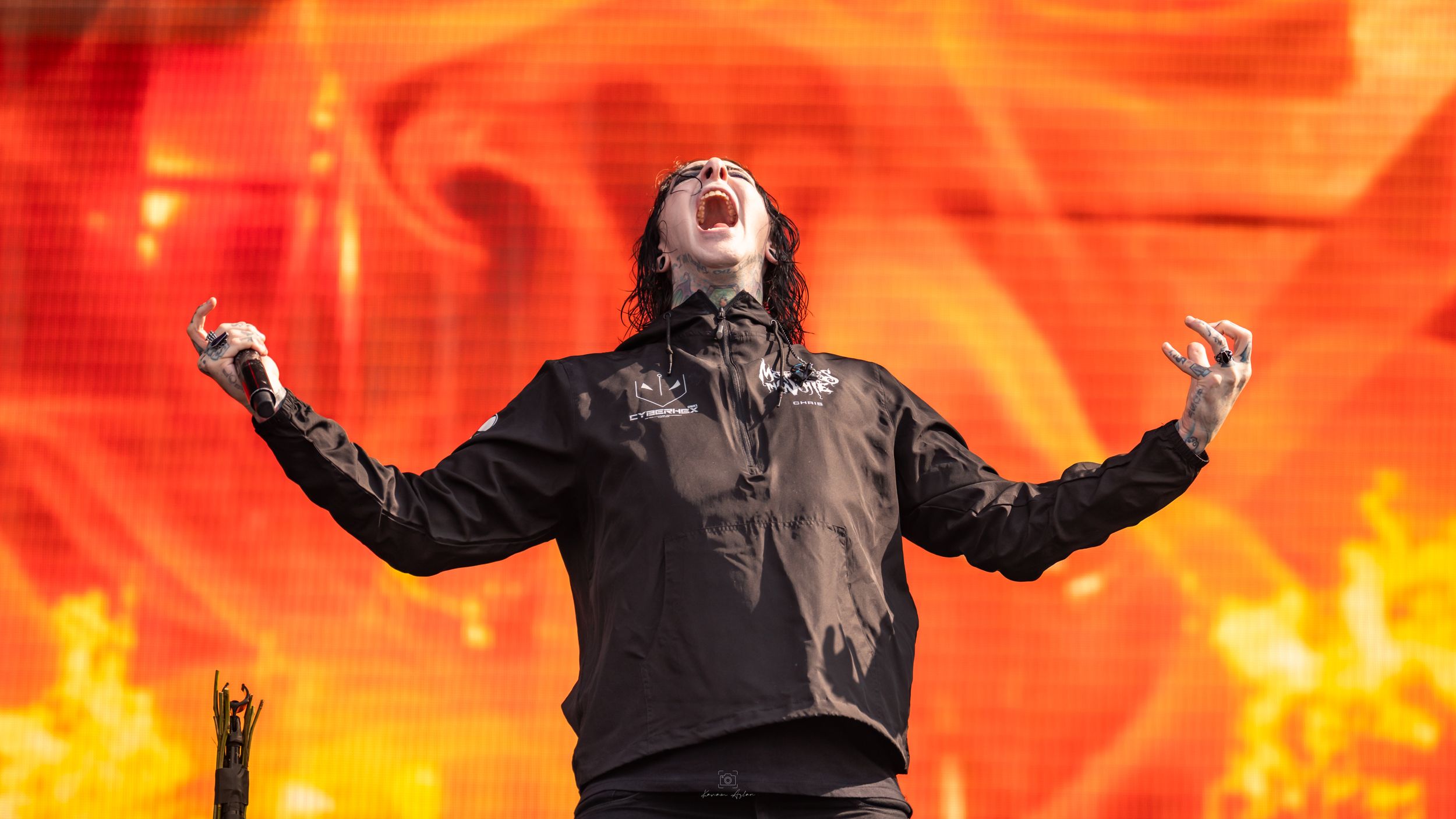 A performer on stage sings passionately against a dramatic backdrop of orange flames and lighting effects.