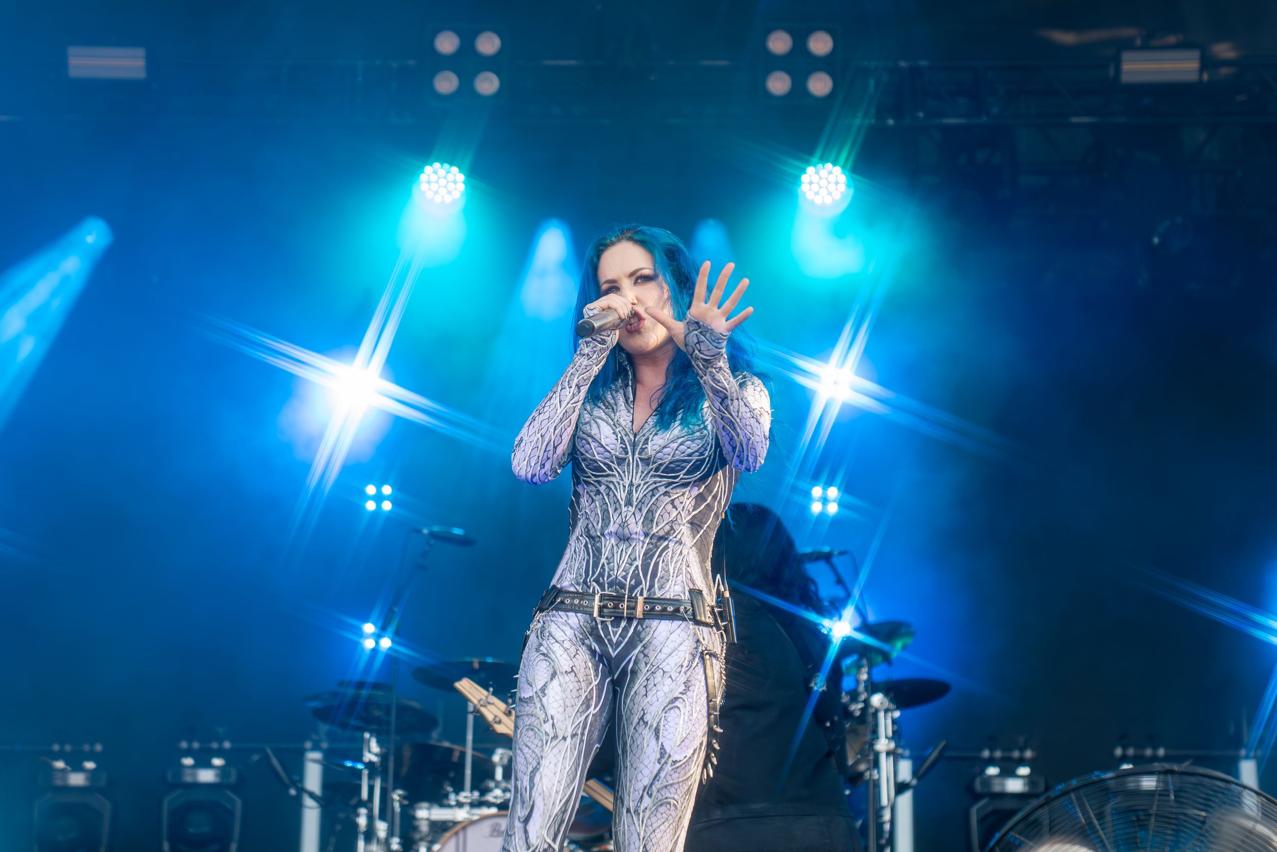A performer in a sparkly silver outfit sings on stage under dramatic blue lighting during a concert performance.