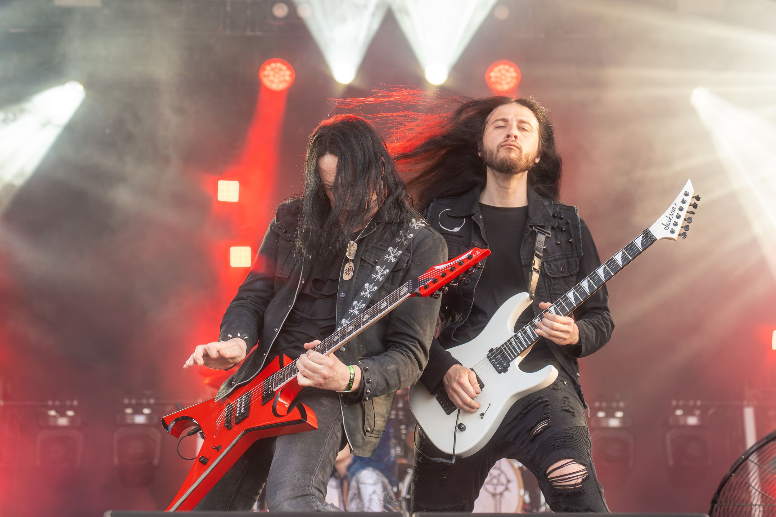 Rock musicians perform on stage with electric guitars amid dramatic red lighting and fog effects during a concert.