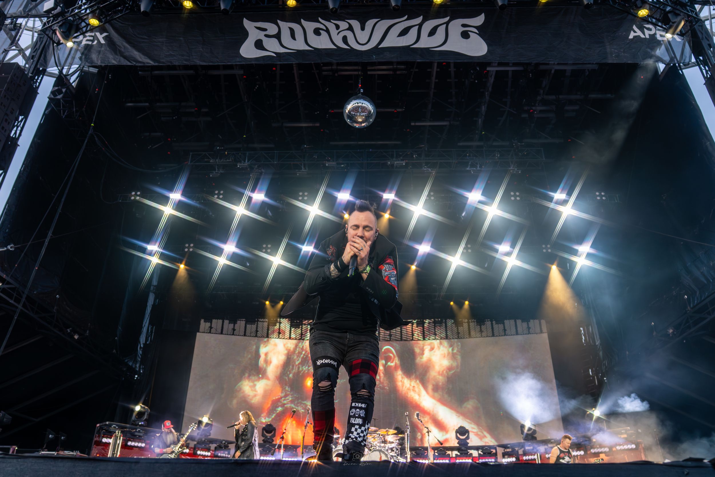 Rock band performs on stage with dramatic lighting and pyrotechnic effects during an energetic concert performance.