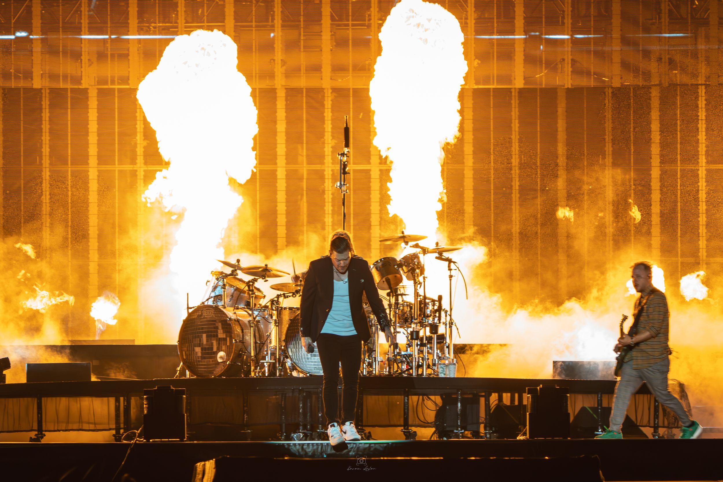 Concert stage illuminated with bright orange flames and spotlights creating a dramatic silhouette effect.