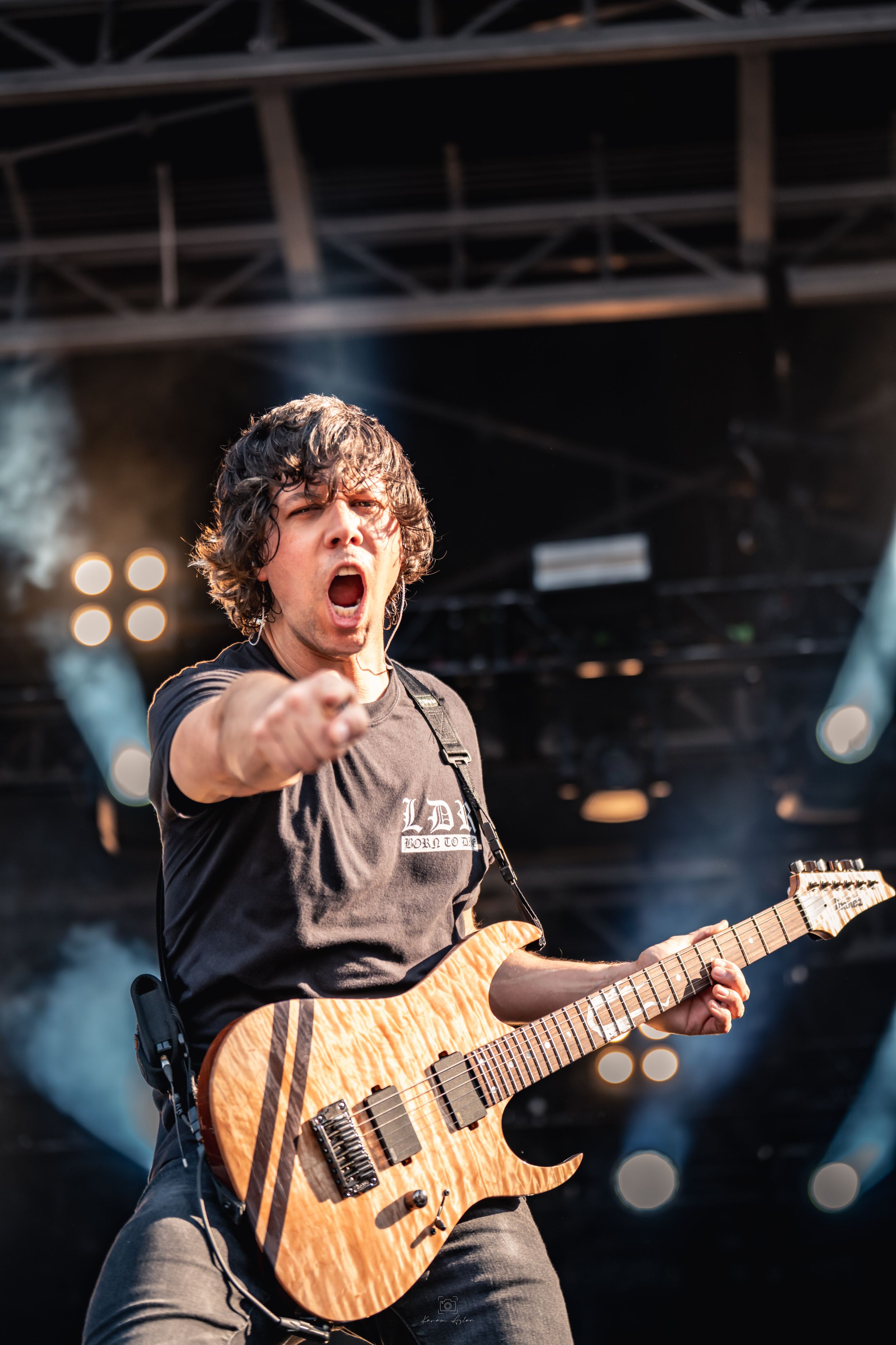 Musician performs passionately on stage with a wooden electric guitar under dramatic concert lighting.