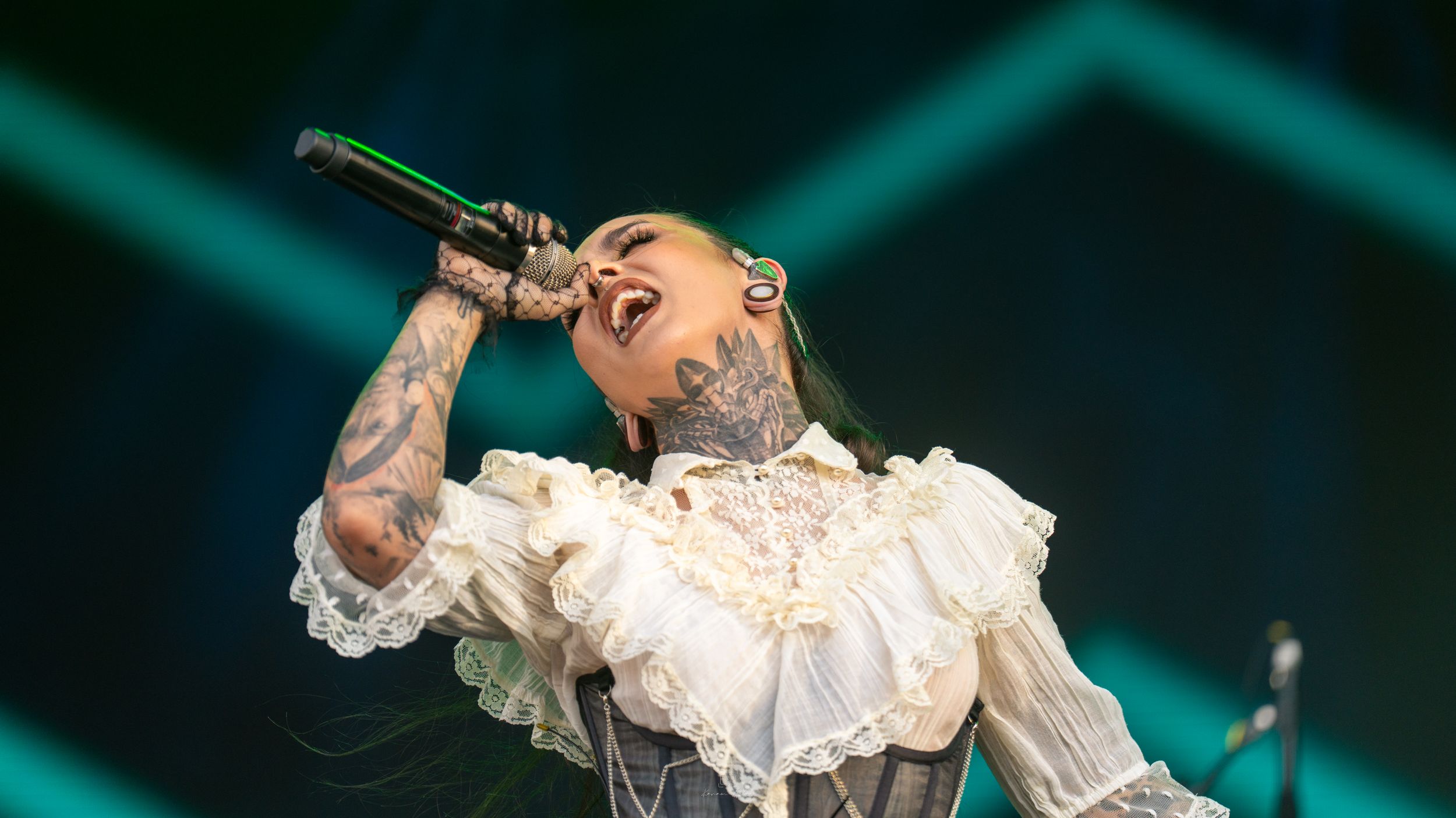 A performer in an ornate white lace dress sings passionately on stage with dramatic lighting effects.