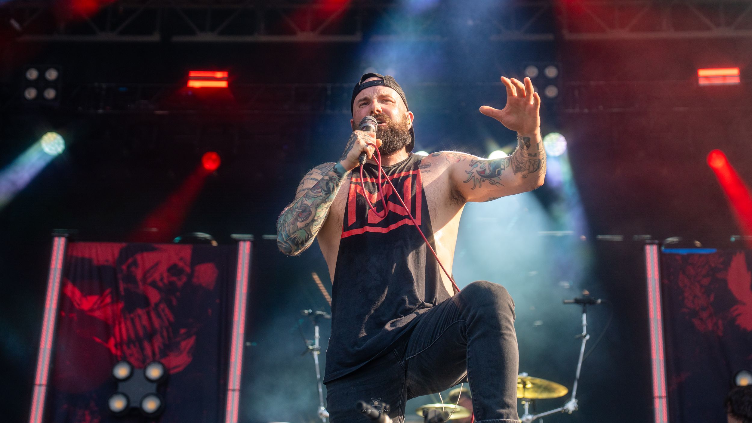 Concert performer energetically singing on stage with dramatic red lighting and smoke effects during live performance.