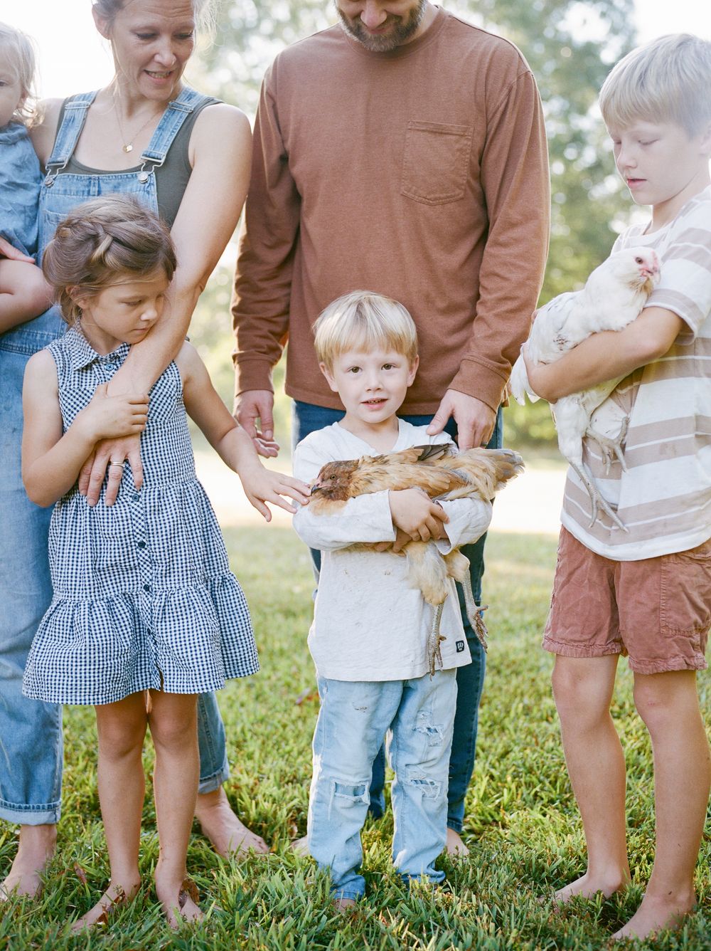 A group gathered outdoors on grass while a young child holds what appears to be a small animal or pet.
