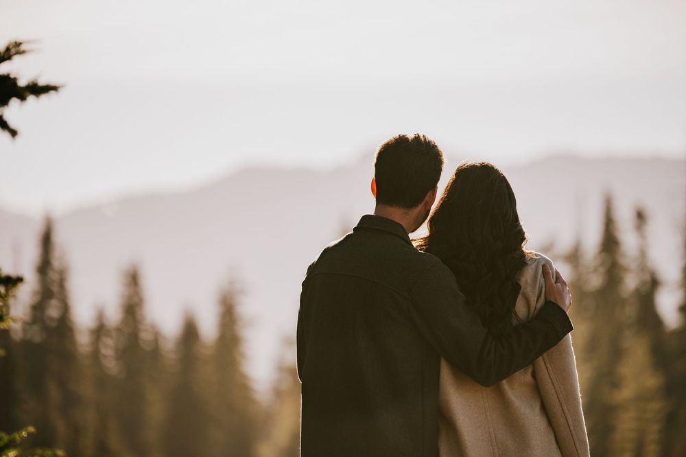 Engagement photographer of couple on Mt. Washington hugging and looking at mountain view in Paradise Meadows for couple photoshoot