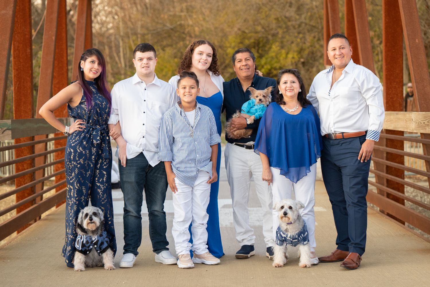 A family group poses with their dogs on a wooden bridge during an outdoor photo session.
