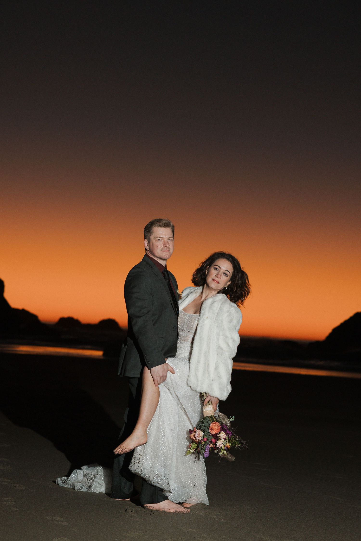 A romantic wedding photo shows a couple embracing under a flowing white veil against a bright blue sky.